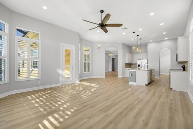 17009 SW Sapri Way, Port Saint Lucie, FL 34986 - unfurnished living room featuring arched walkways, ceiling fan, light wood finished floors, recessed lighting, and a sink