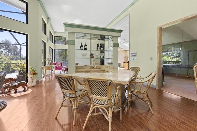 dining space with wood finished floors, baseboards, ornamental molding, bar, and a high ceiling