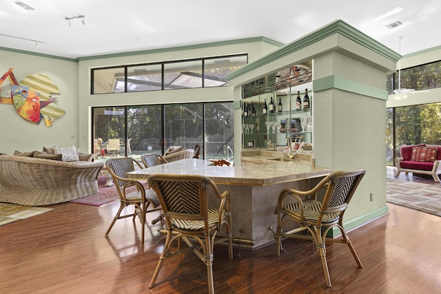 dining area featuring wood finished floors, wet bar, and ornamental molding