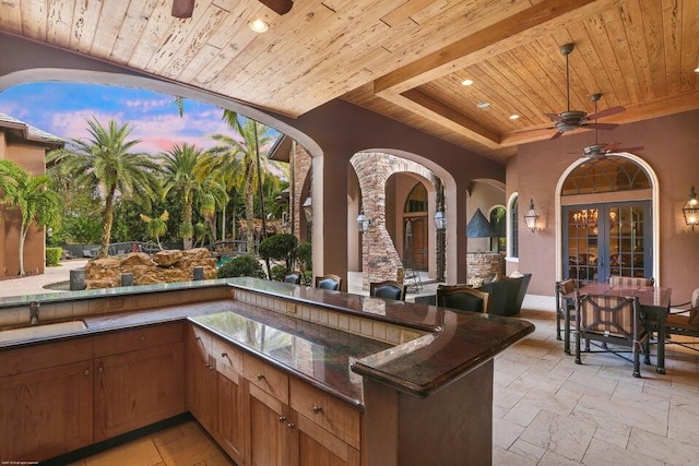 patio terrace at dusk with an outdoor kitchen, french doors, ceiling fan, and a sink