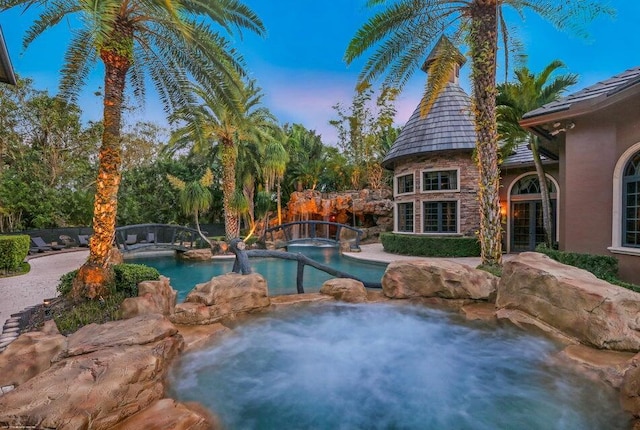 pool at dusk featuring a patio and a pool with connected hot tub
