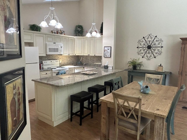 kitchen featuring white appliances, a chandelier, a peninsula, wood finished floors, and a towering ceiling