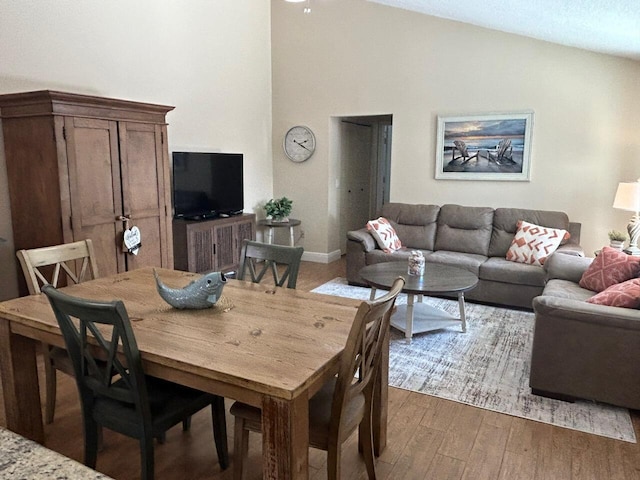 dining space with wood finished floors and high vaulted ceiling