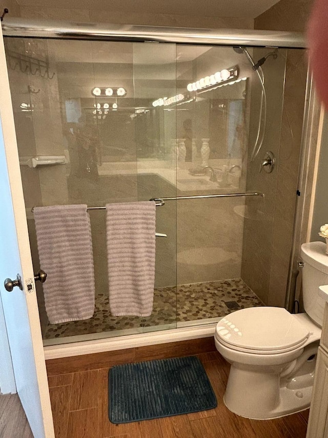 bathroom with toilet, wood finished floors, and a stall shower