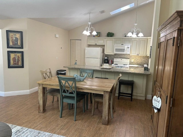 dining room featuring a chandelier, light wood finished floors, lofted ceiling, baseboards, and a skylight