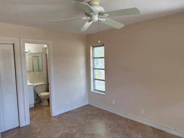 unfurnished bedroom with a closet, baseboards, ensuite bathroom, and a ceiling fan