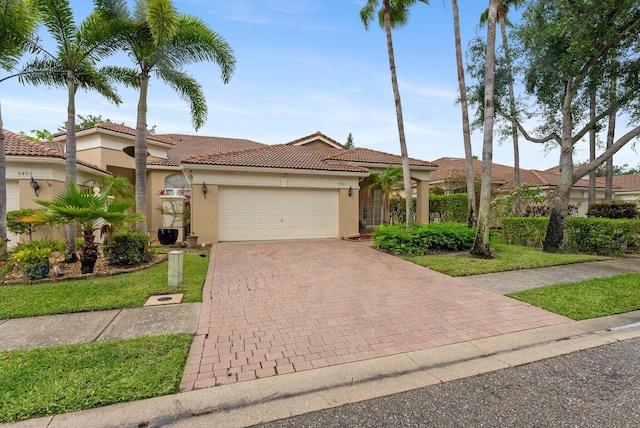 mediterranean / spanish house with a tiled roof, stucco siding, a garage, and decorative driveway