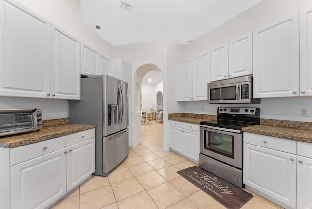 kitchen with stainless steel appliances, arched walkways, white cabinetry, and light tile patterned flooring