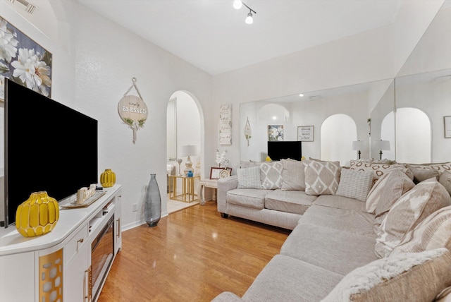 living room featuring arched walkways, light wood-style flooring, and baseboards