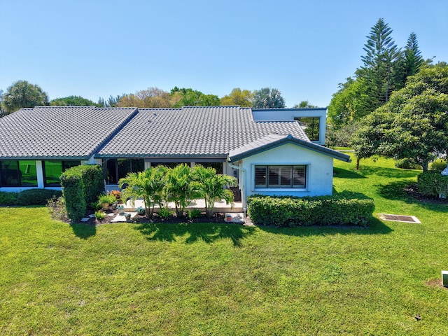 back of house with a tiled roof, a lawn, and stucco siding