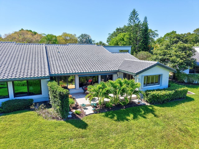 rear view of property with a patio area, a tiled roof, and a lawn