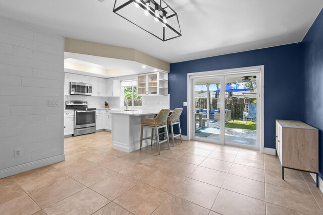 kitchen featuring stainless steel appliances, light tile patterned floors, white cabinets, a kitchen bar, and light countertops