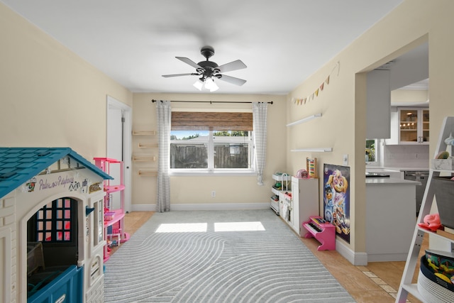 playroom with ceiling fan and baseboards