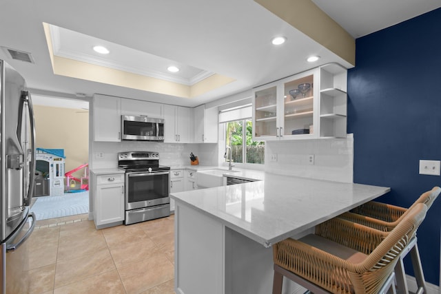 kitchen featuring appliances with stainless steel finishes, a sink, ornamental molding, a peninsula, and a tray ceiling