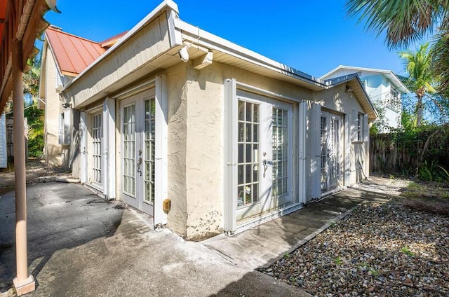 341 NE 7th Ave, Delray Beach, FL 33483 - view of side of home with french doors, stucco siding, a patio area, fence, and metal roof