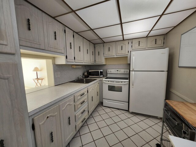 kitchen featuring white appliances, a sink, light countertops, light tile patterned flooring, and a drop ceiling