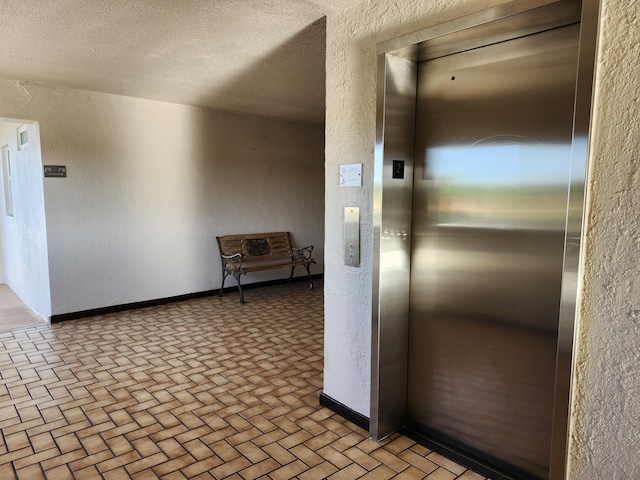 hallway featuring elevator, a textured wall, and brick patterned floors