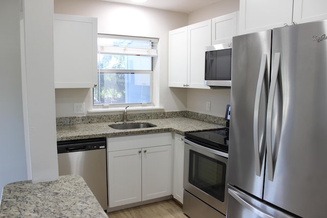 kitchen featuring appliances with stainless steel finishes, a sink, white cabinets, light stone counters, and light wood-style flooring