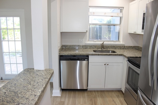 kitchen featuring appliances with stainless steel finishes, a sink, white cabinetry, light stone countertops, and light wood-style flooring
