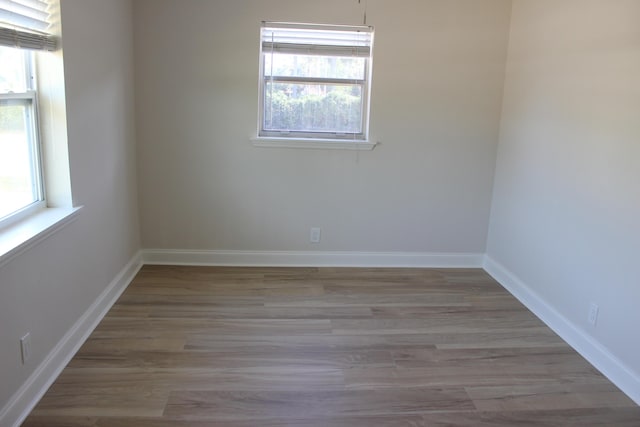 unfurnished room with healthy amount of natural light, wood finished floors, and baseboards