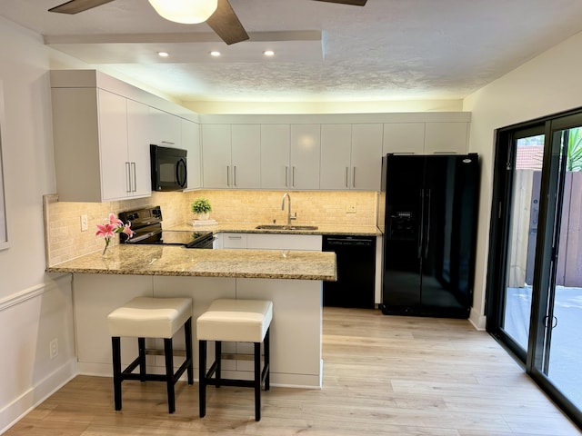 3400 Spanish Wells Dr Unit 52-C, Delray Beach, FL 33445 - kitchen with black appliances, a sink, a peninsula, decorative backsplash, and light wood-style floors