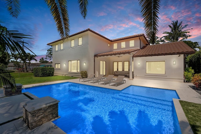 12891 Inshore Dr, Palm Beach Gardens, FL 33410 - back of house at dusk featuring a tiled roof, a patio, stucco siding, a ceiling fan, and a lawn