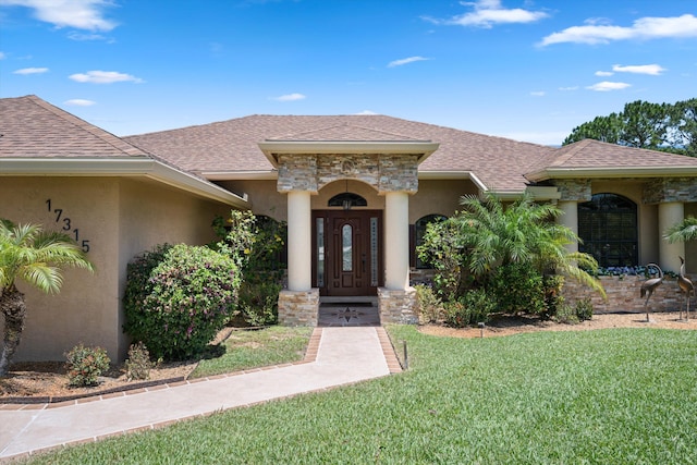 17315 Orange Blvd, Loxahatchee, FL 33470 - view of exterior entry with a yard, a shingled roof, and stucco siding