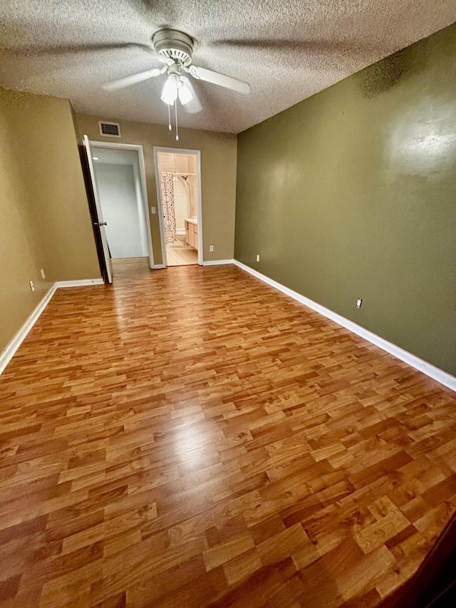 empty room with a ceiling fan, wood finished floors, baseboards, and a textured ceiling