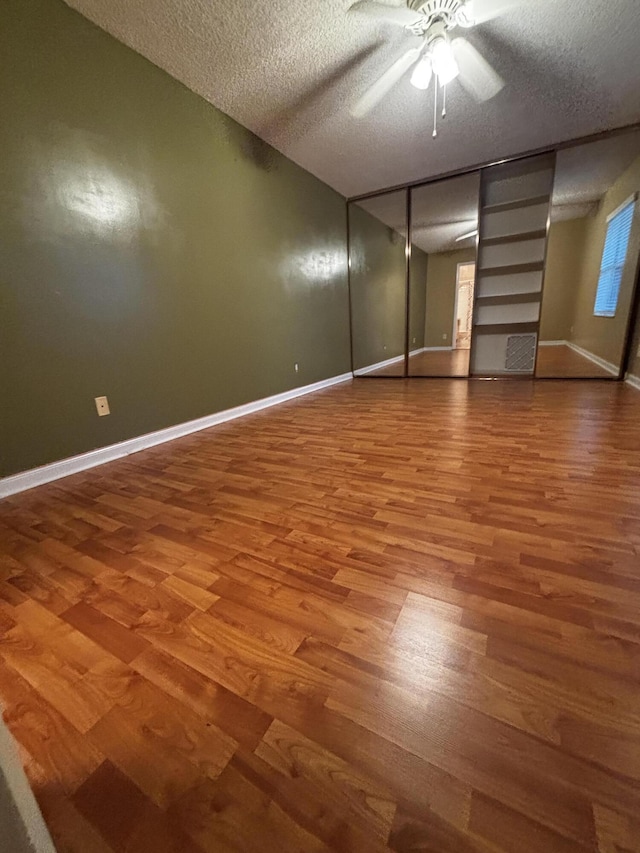 unfurnished bedroom with a textured ceiling, wood finished floors, baseboards, and ceiling fan