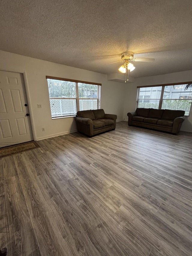 living area featuring a textured ceiling, dark wood finished floors, plenty of natural light, a ceiling fan, and baseboards