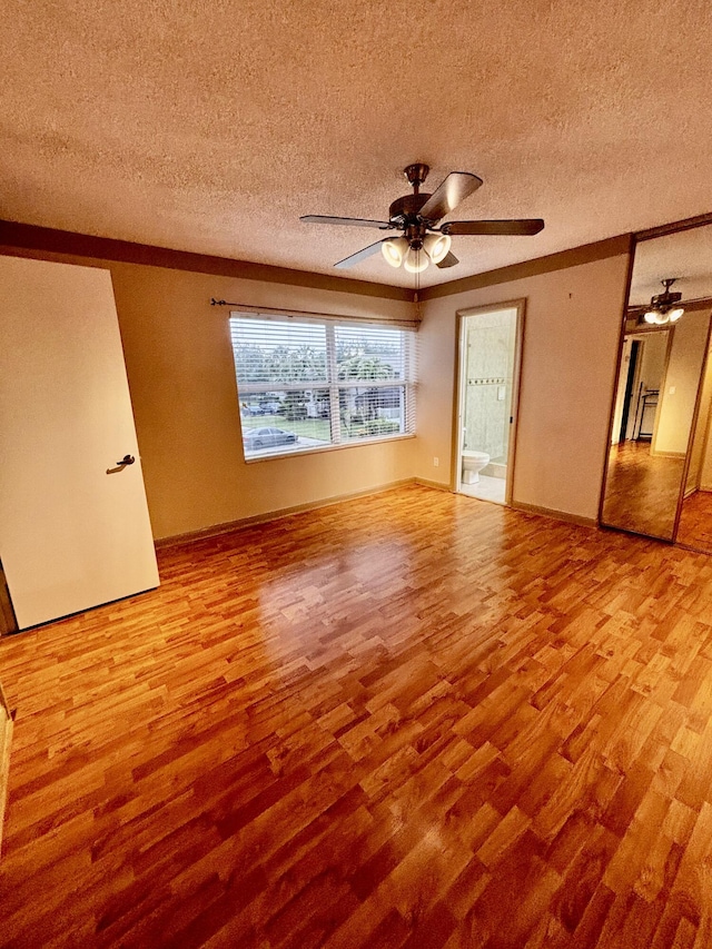 unfurnished bedroom with wood finished floors, a textured ceiling, crown molding, baseboards, and ensuite bath