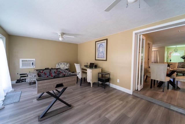 playroom with ceiling fan, a wall unit AC, wood finished floors, baseboards, and a textured ceiling