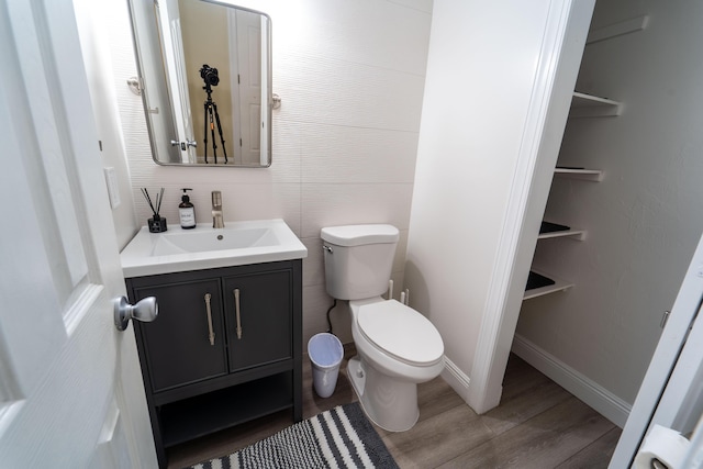 half bathroom featuring wood finished floors, toilet, vanity, and baseboards