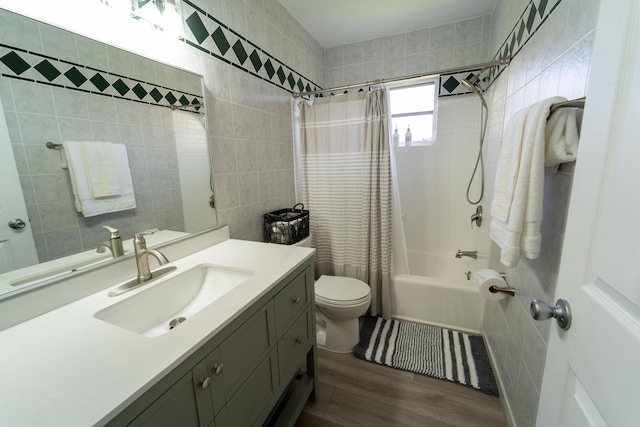 full bath with tile walls, wood finished floors, shower / tub combo with curtain, toilet, and vanity