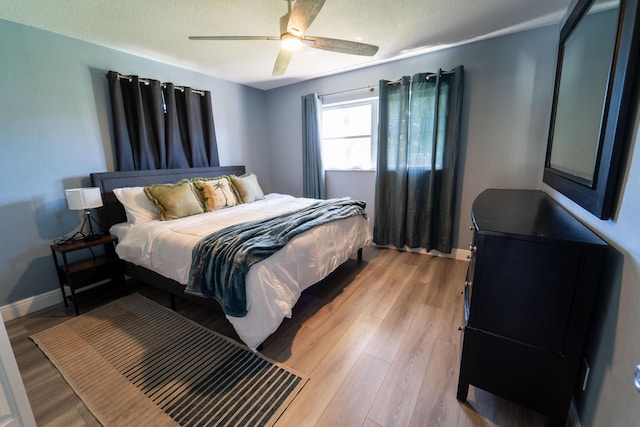 bedroom featuring light wood-type flooring, a textured ceiling, ceiling fan, and baseboards