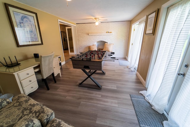 playroom with wood finished floors, a ceiling fan, brick wall, baseboards, and an office area