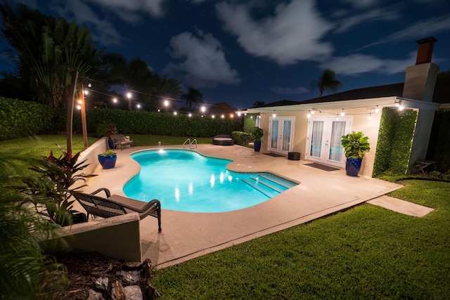 pool at night featuring french doors, a patio area, and a yard