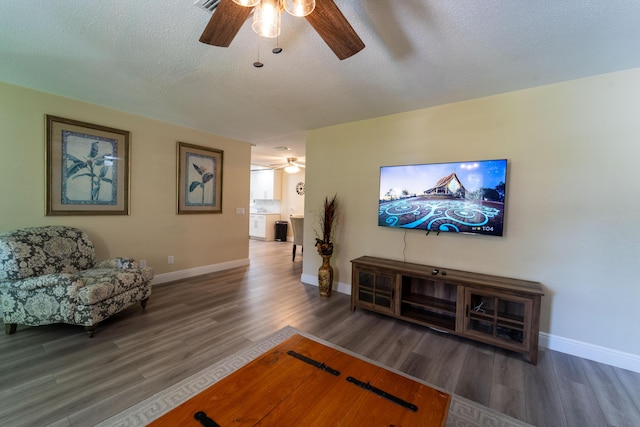 living room with a ceiling fan, wood finished floors, baseboards, and a textured ceiling