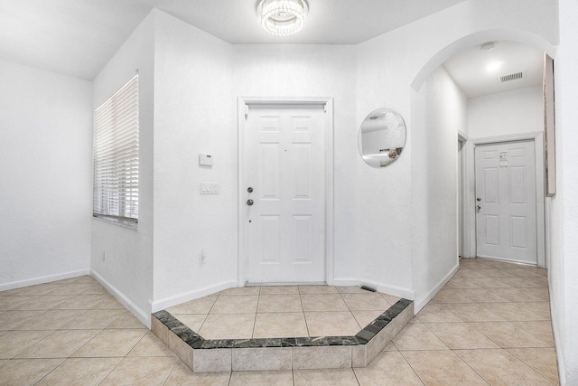 entryway featuring arched walkways, light tile patterned floors, and baseboards