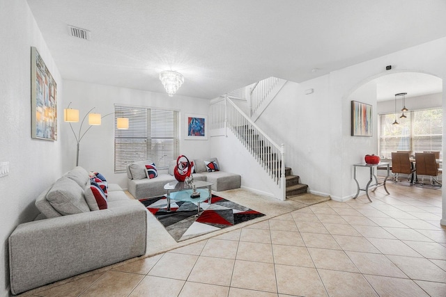 living area featuring arched walkways, tile patterned floors, stairs, and a chandelier