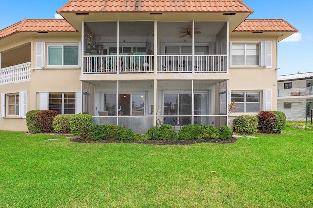 back of house featuring a tile roof, stucco siding, a ceiling fan, and a lawn