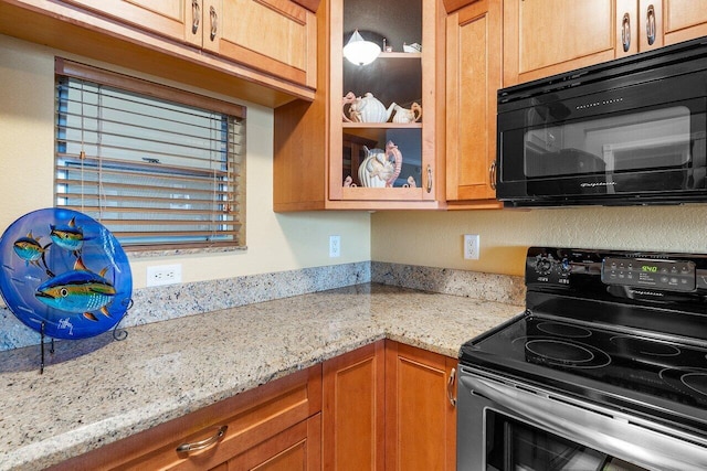 kitchen with electric stove, black microwave, light stone countertops, glass insert cabinets, and brown cabinets