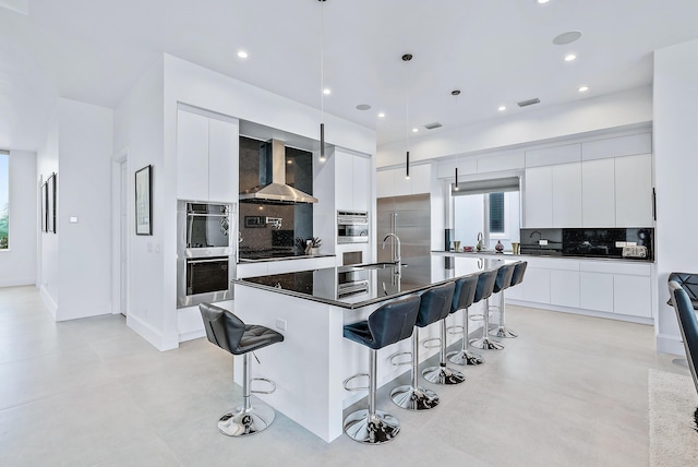 kitchen featuring modern cabinets, wall chimney exhaust hood, a breakfast bar area, decorative backsplash, and white cabinetry