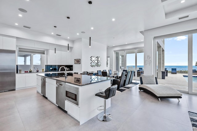 kitchen featuring modern cabinets, a sink, dark countertops, stainless steel appliances, and a kitchen island with sink
