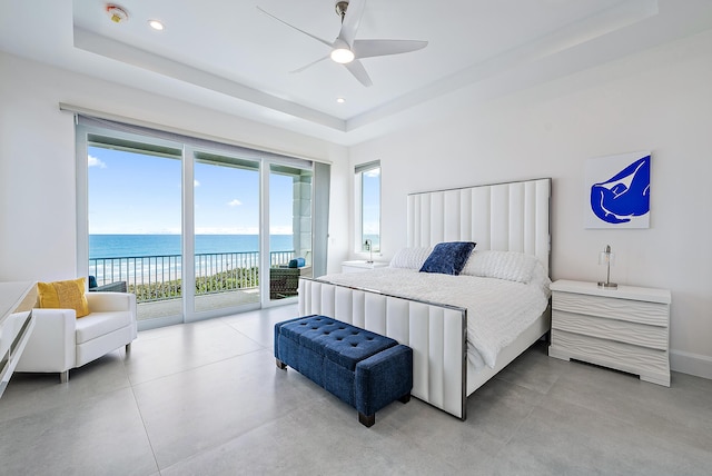 bedroom with a tray ceiling, access to exterior, a water view, recessed lighting, and a ceiling fan