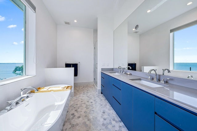 full bath featuring double vanity, a freestanding bath, a shower stall, recessed lighting, and a water view