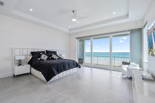bedroom featuring a raised ceiling, access to outside, concrete flooring, a water view, and ceiling fan