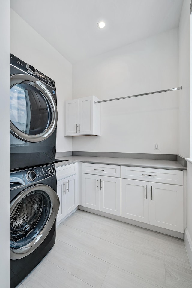 laundry room with estacked washer and dryer, cabinet space, recessed lighting, and light wood-type flooring