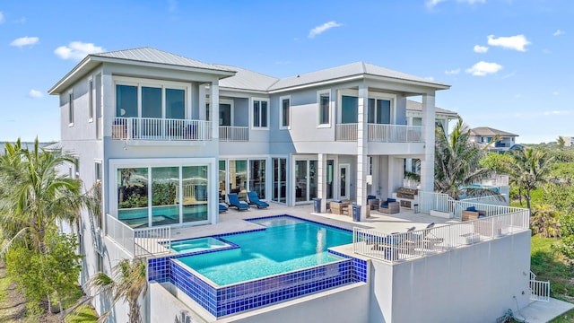 back of property with a balcony, a patio, a pool with connected hot tub, metal roof, and an outdoor hangout area