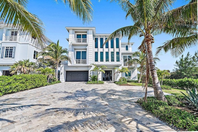 beach home with a balcony, decorative driveway, an attached garage, and stucco siding
